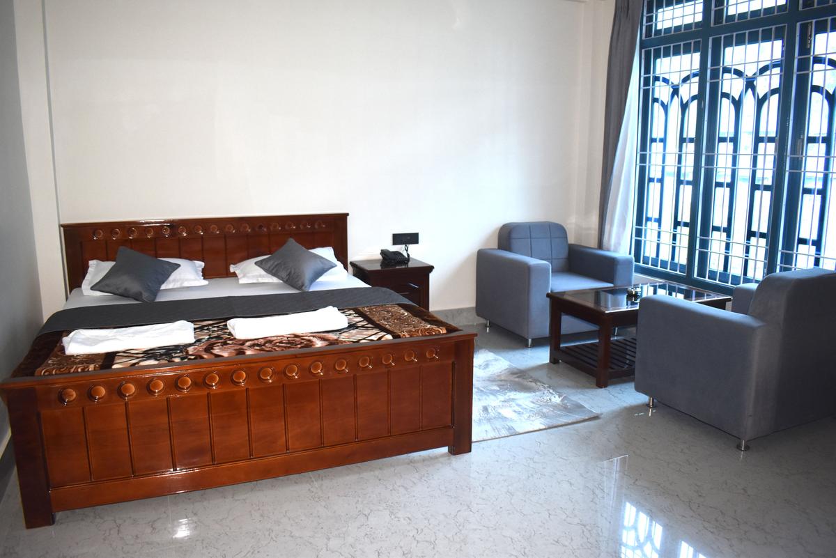 Deluxe Room Rs 5000 with king bed and grey sofa chairs at Hotel Pema Lhatse Dirang